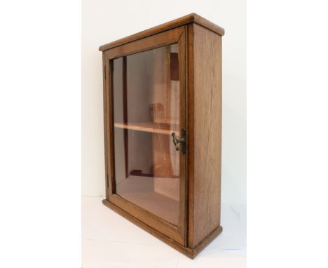 A heavy Edwardian oak wall-hanging display cabinet: canted corners and the single glazed door enclosing a velvet lined interi