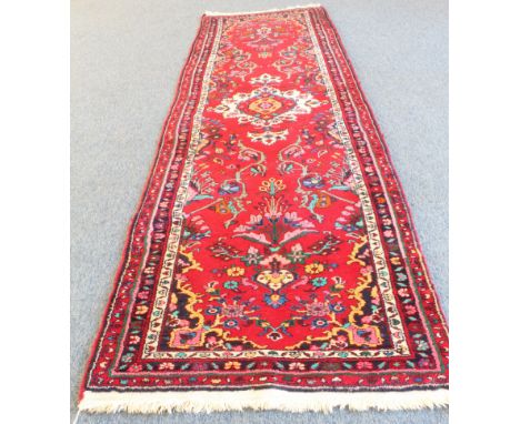 A Persian Hamadan runner; red ground with ivory central medallion and sprays of flowers surrounded by three borders (318 x 87