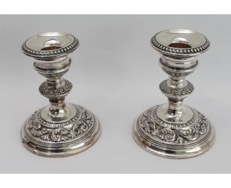 A pair of modern, hallmarked silver, weighted candlesticks: spreading circular feet decorated with scrolling foliage; maker's