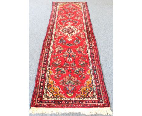 A Persian Hamadan runner; red ground with ivory central medallion surrounded by flowers (294 x 89 cm) * Condition: Good  