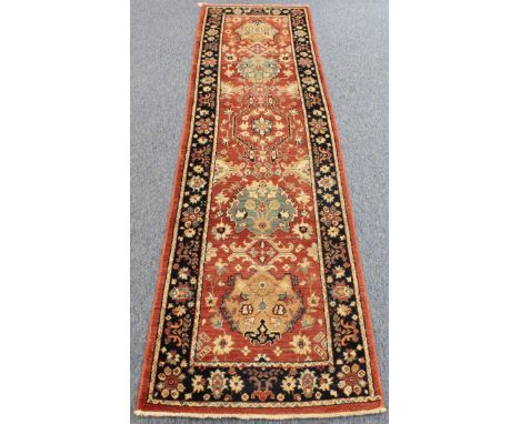 A Kashmir runner; terracotta field containing five lozenges surrounded by a dark-blue floral border (292 x 79 cm).