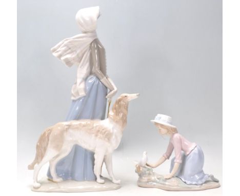 Lladro - A large porcelain figure of a 1920's lady wearing a bonnet and scarf walking her long hair greyhound dog and holding