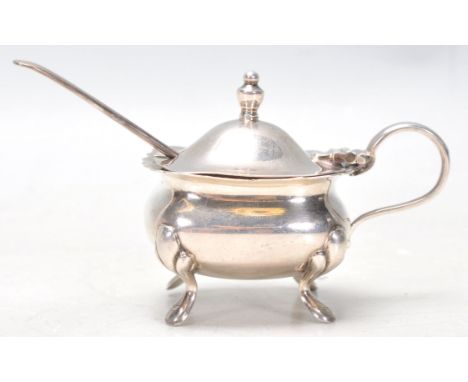 A hallmarked Sterling silver mustard pot set upon four figured&nbsp;feet with a hinged lid and finial with liner and spoon in