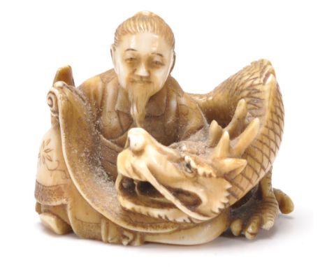 An antique Chinese ivory Netsuke toggle intricately carved in the form of a seated man in traditional robes with a four toed 