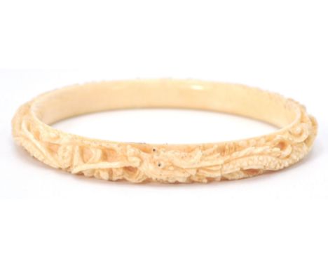An antique early 20th Century Chinese finely carved ivory bangle with a repeating dragon motif.