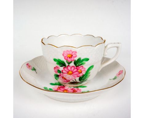 A white porcelain teacup and saucer that are painted with pink flowers and decorated with a gold trim. Herend backstamp. Dime