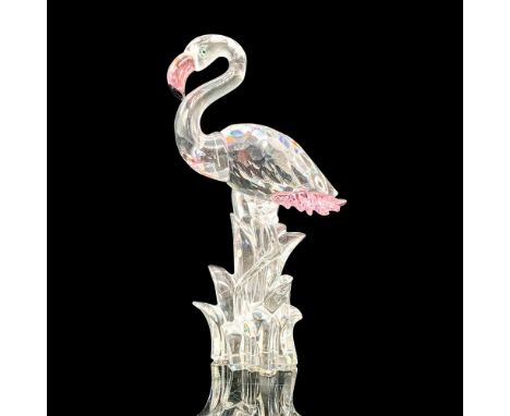 A clear crystal figure of a flamingo with pink crystal accents standing on one leg in some tall grass. Swarovski backstamp. T