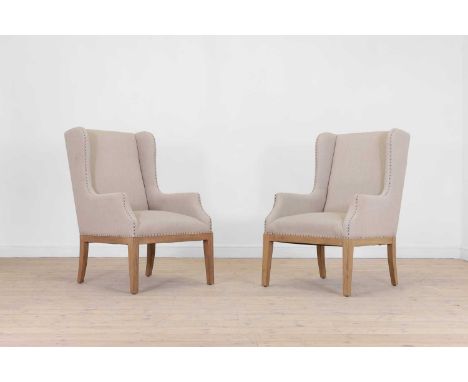 A pair of oak wingback armchairs by OKA, of recent manufacture, each with pale studded upholstery, raised on tapering square 