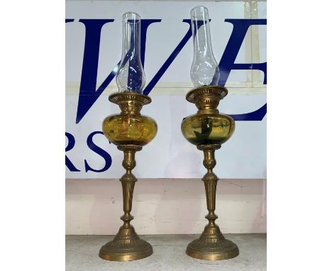 A pair of brass column oil lamps with amber glass reservoirs and chimneys 
