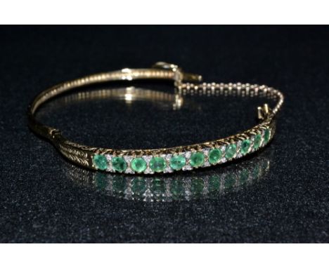 A 9ct gold diamond & green stone hinge bangle, eleven round cut green stones, each divided by a pair of diamond accents, 9ct 