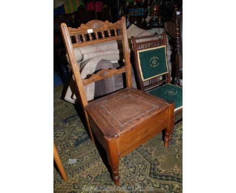 An Edwardian Oak Commode Chair with carved and shaped top rail with spindle turned supports, lifting bergere seat, deep friez