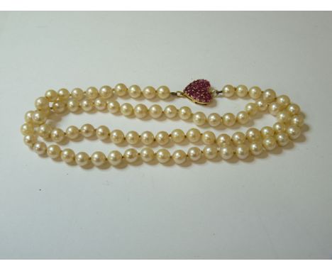A single row uniform cultured pearl necklace, with a heart shaped ruby cluster station, tested as approximately 14ct gold
