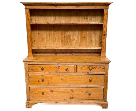A Victorian pine dresser. The upper section with two shelf racks on a drawer base with three short and two long on bracket fe
