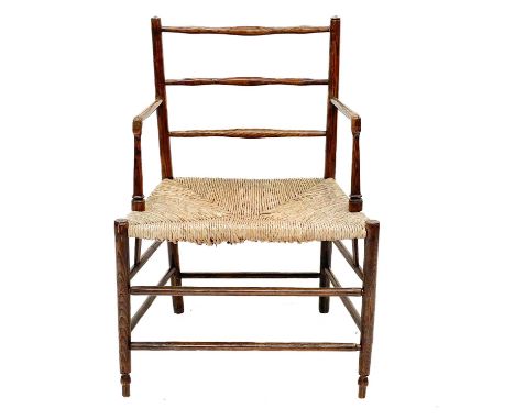 A 19th century Sussex ash elbow chair. With adze carved ladder back over a rush seat on tapering splayed supports and stretch