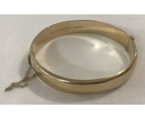 A 9ct gold hinged bangle with safety chain. Total weight 13.4g. 