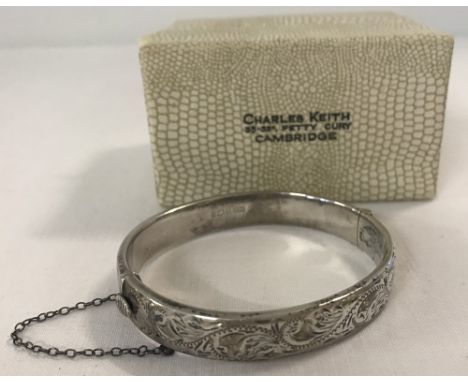 A silver hinged bangle complete with safety chain and original box. Engraved detail to one half. Hallmarked Birmingham 1970. 