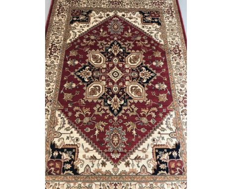A Heriz pattern rug; red background with blue, beige and gold colouration. Tasselled ends. Approx. 230cm x 160cm.