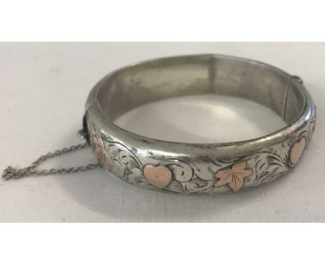 A silver hinged bangle with gold heart and ivy leaf decoration, complete with safety chain. Hallmarked Sheffield 1952. 