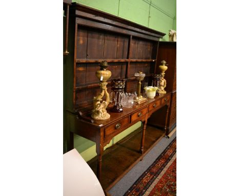 A George III oak dresser, with plate rack back, the base fitted with four drawers above a boarded pot shelf, 199cm by 50cm by