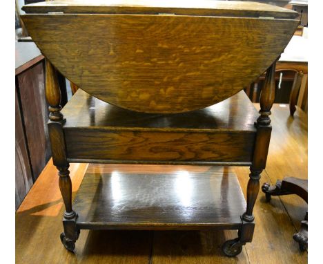 An early 20th century oak dinner wagon, with two rounded drop leaves above spindle supports, fitted with a shelf, 61cm wide  