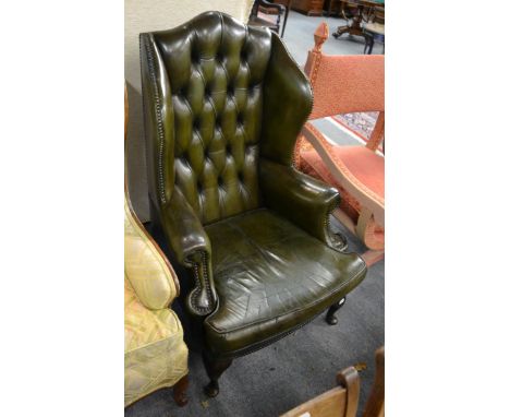 A George III style studded green leather button back wing armchair, raised on cabriole legs, on pad feet      