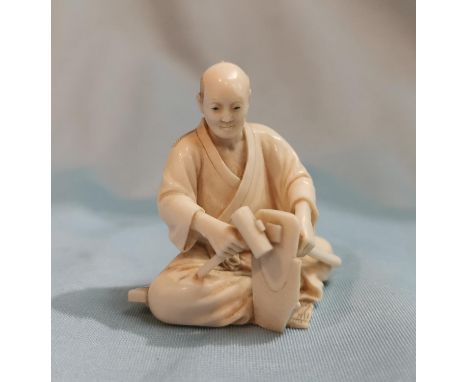 A late 19th / early 20th century Japanese early 20th century carved Ivory miniature Okimono figure of a man seated with tools