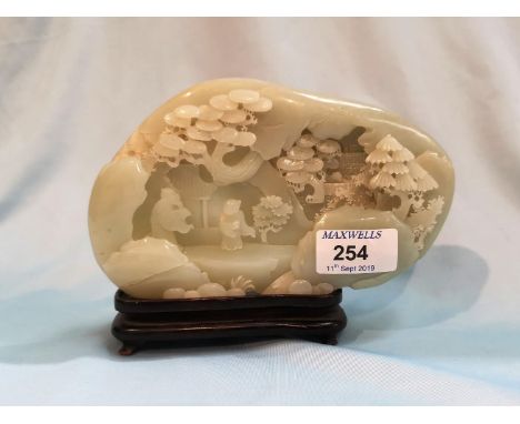 A Chinese jade coloured hardstone carving depicting figures and trees in front of a cave, length 7"