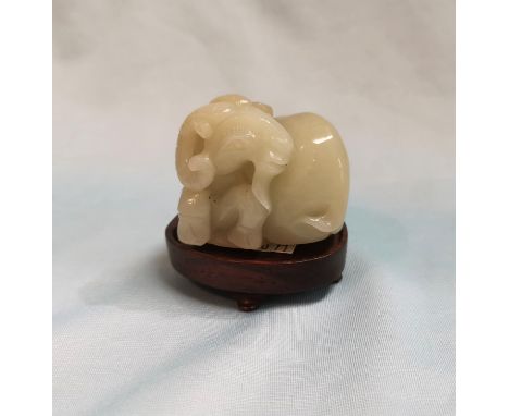 A Chinese jade coloured hardstone carving depicting a reclining goat, length 2", on hardstone base