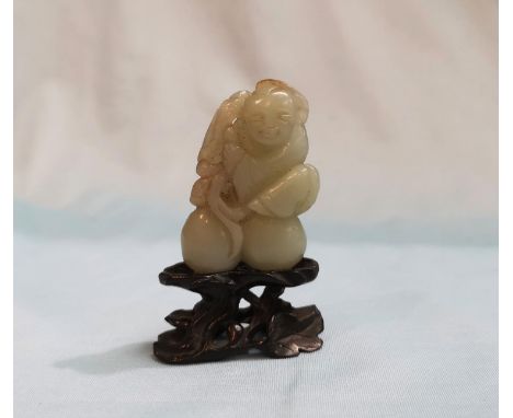 A Chinese jade coloured hardstone carving depicting a seated figure, height 2", on hardwood base