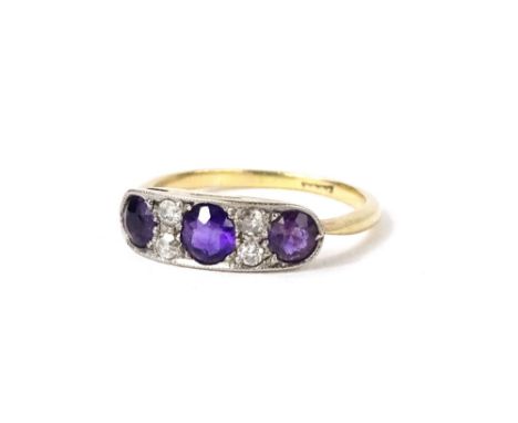 A amethyst and diamond Art Deco style dress ring, set with three amethyst round brilliant cut stones, with two tiny diamonds 