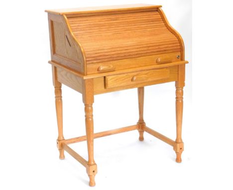 An Ercol type light oak roll top desk, the tambour door enclosing a fitted interior with brass handles, above a frieze drawer