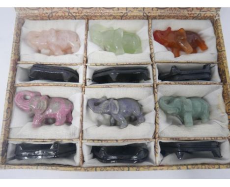 A Chinese, boxed set of six, hand-carved hardstone elephants, each with hardwood stands to include a jade and rose quartz exa