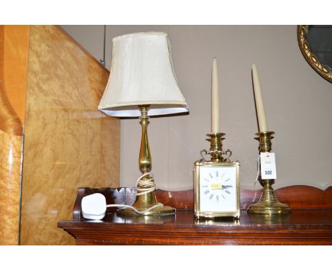 A pair of antique brass candlesticks; a brass table lamp with cream coloured shade and a carriage clock with quartz movement.