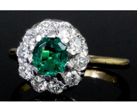 A modern 18ct gold mounted emerald and diamond flowerhead ring, the central cushion cut emerald of .63ct surrounded by ten br