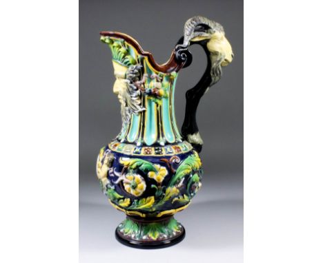 A 19th Century Continental majolica ewer moulded with two Putti supporting a cartouche, acanthus leaves and fruit, the neck w