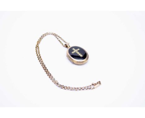 A Victorian oval yellow metal locket, the black enamel front set with seed pearl crucifix, the reverse with engraved buckle c