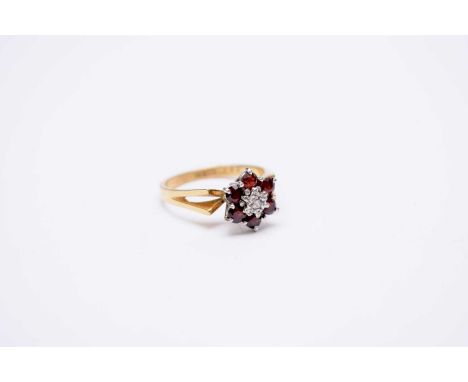 A garnet and diamond floral cluster ring, designed as a central faceted diamond claw set within a border of six round mixed c
