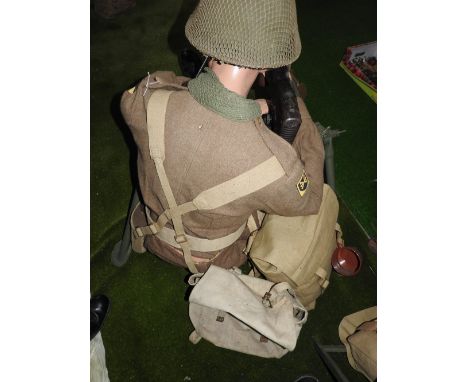 A seated mannequin in a khaki uniform insignia for, along with webbing, helmet, boots, supply bags, etc