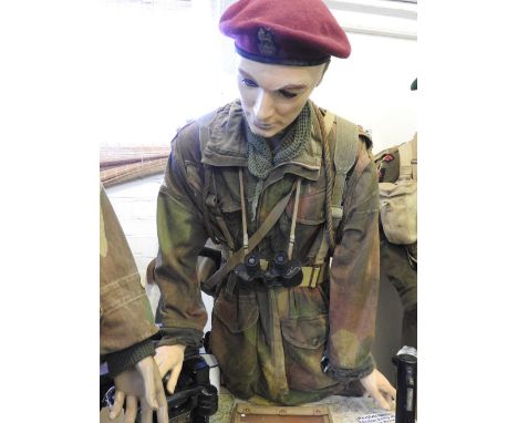 A standing mannequin leaning forward in khaki wearing a red beret, wearing Denison Smock, face veil, boots, an entrenching to