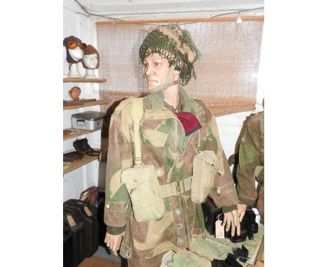 A standing mannequin wearing camouflage uniform with webbing water bottle and trenching in tool his red beret tucked into the