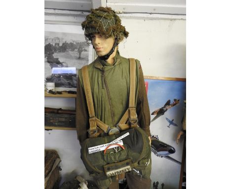 A standing mannequin wear Parachute Regiment jump jacket, camouflage helmet and dummy parachute pack with field dressings etc