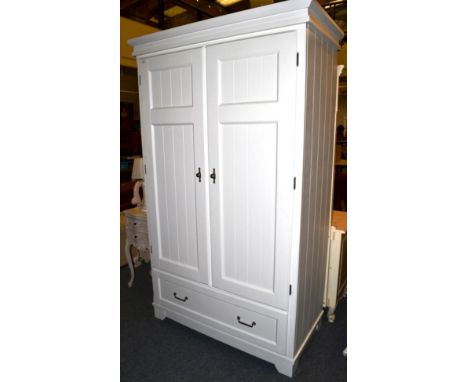 A White Painted Double Door Wardrobe of recent date, panel doors enclosing a hanging rail and shelf with a long drawer, chrom