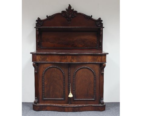 A William IV serpentine front chiffonier, the carved crest above a shelf, the base fitted twin arch panel doors, ripple mould