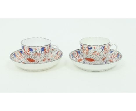 A pair of English porcelain teacups and saucers, circa 1800, painted blue and red, heightened in silver with flowers