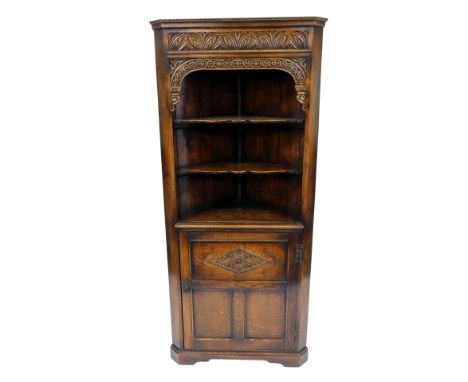 An Old Charm style oak corner display cabinet, with a pediment over a carved frieze, over two shaped shelves above a carved p