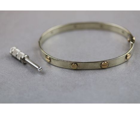 A 9ct gold hinged bangle in the style of Cartier, pale yellow tone with yellow screw motifs, width approximately 6mm, the cla