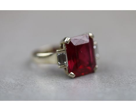 A synthetic ruby and diamond yellow gold ring, the large central rectangular mixed cut synthetic ruby with baguette cut diamo