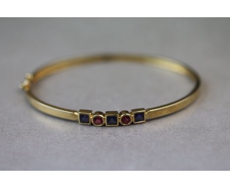 A tanzanite and pink tourmaline 9ct yellow gold hinged bangle, three alternate square step cut tanzanite and two round mixed 