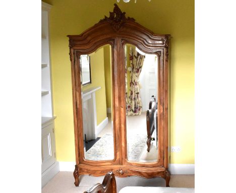 A reproduction French style armoire with mirrored doors and shaped top revealing two shelves, the centre shelf hosting two si