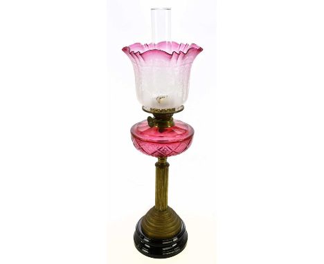 A Victorian oil lamp with clear and cranberry glass shade, etched with decoration of floral sprays, above the cut cranberry g